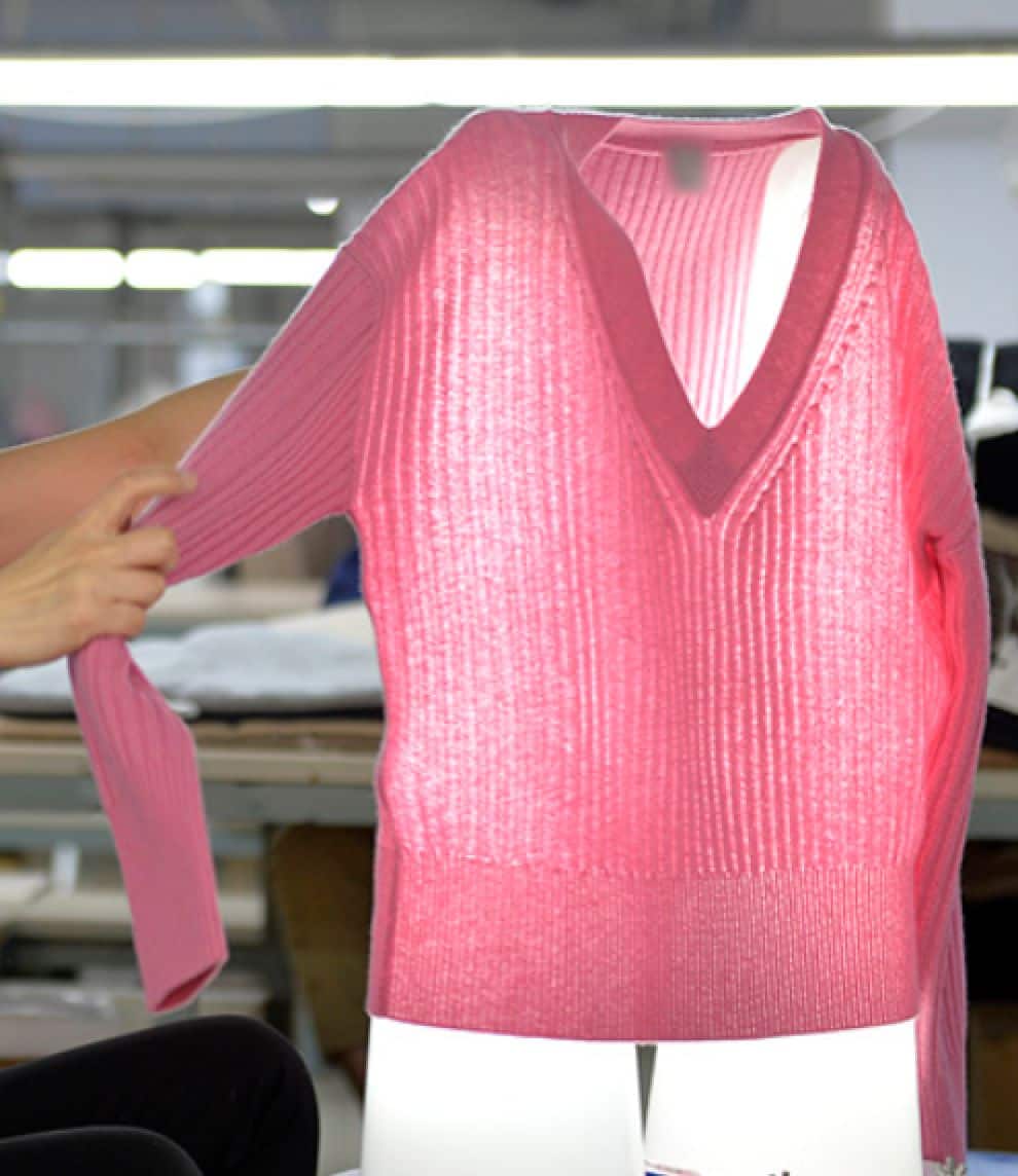 Pink rib V-neck sweater checked over a light board for holes and dropped stitches